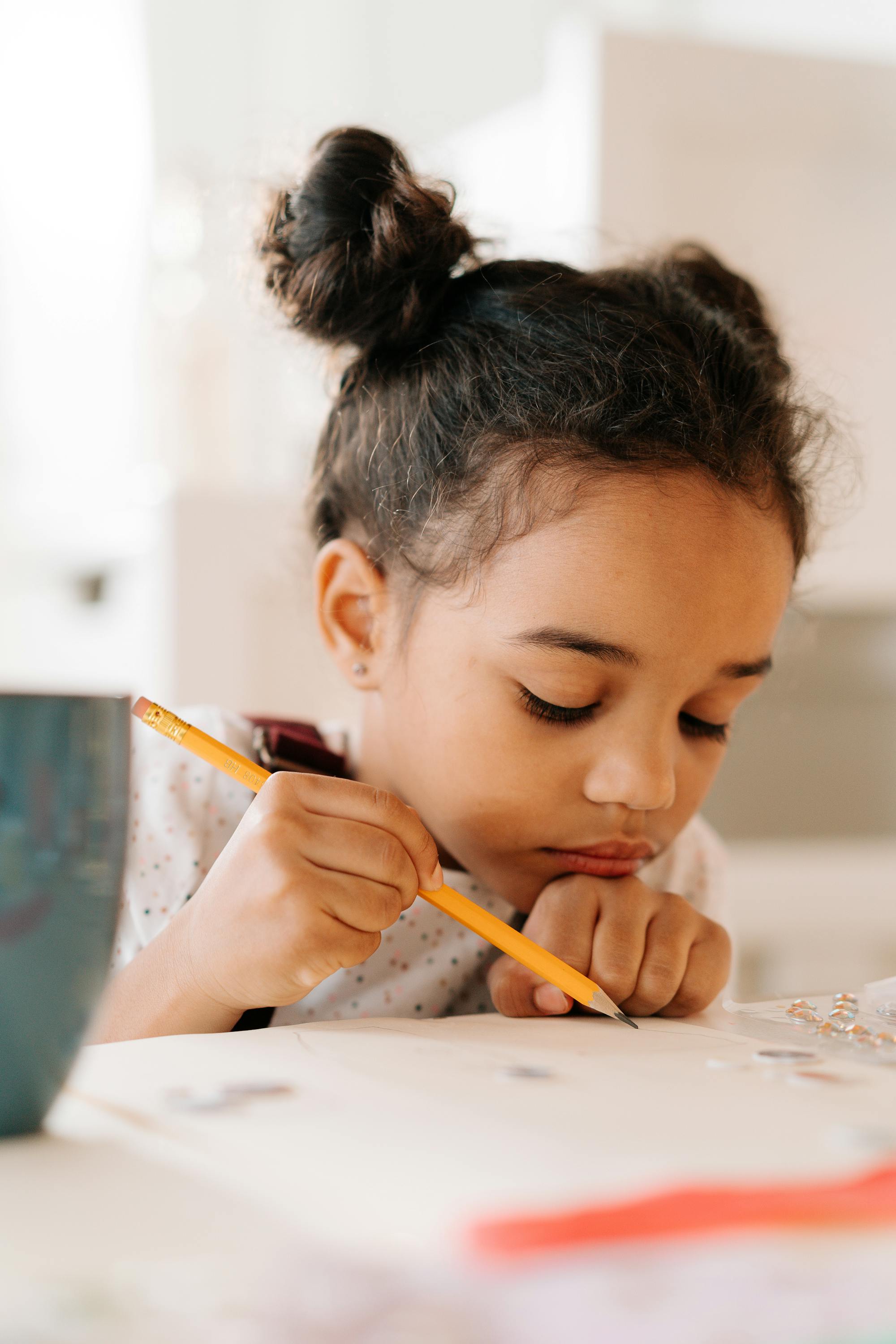 Young girl writing with a pencil at a table, representing education supported through the Crowned Hearts™ Impact initiative. 